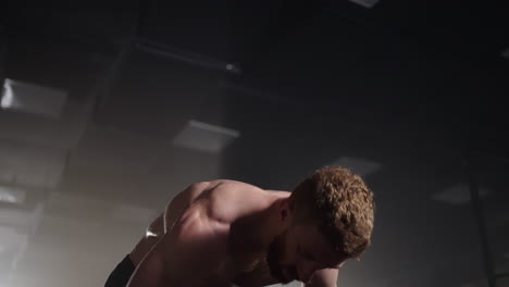 exhausted muscular man raises his head and looks into camera. he's covered in sweat and tries to catch a breath. exhausted male athlete is resting after training workout in gym