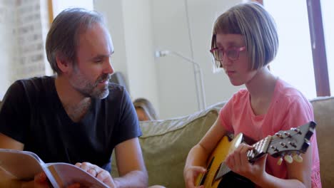 father helping her daughter to play guitar in living room 4k