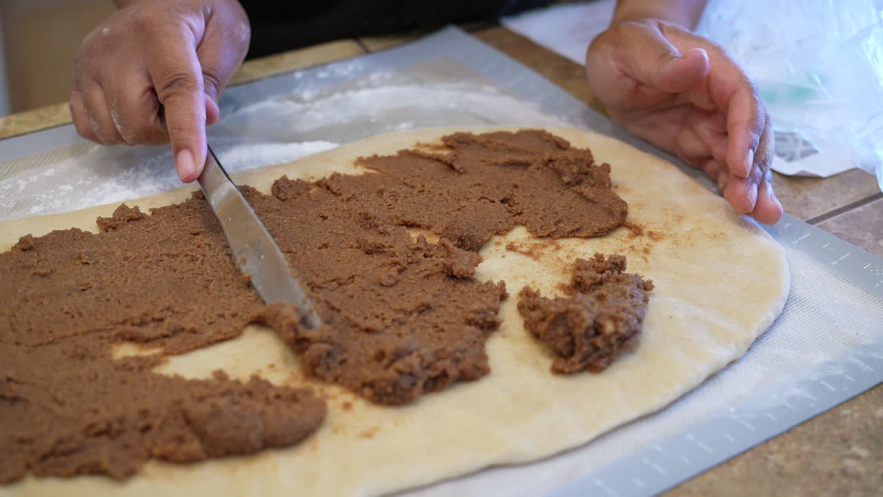 выкладывание на тесто начинки из корицы и коричневого сахара для приготовления вкусных сладких булочек - вид сбоку в замедленном режиме