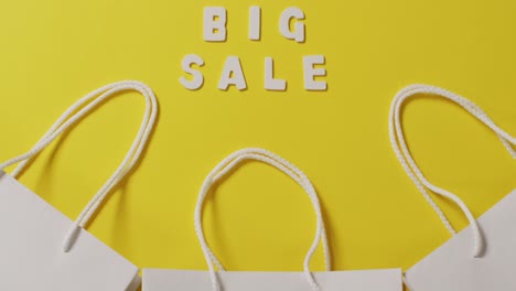 big sale text in white and gift bags with string handles on yellow background