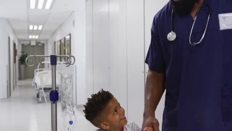 african american male doctor walking with child patient at hospital