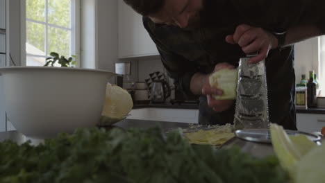 Dolly-shot-of-male-grating-cabbage-in-kitchen-countertop,-ingredients-for-fermentation-process