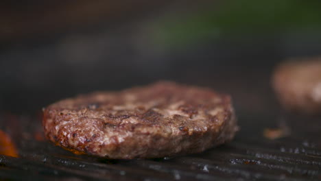 Close-up,-fresh,-juicy-hamburger-patty-cooking-over-a-flaming-barbecue-grill