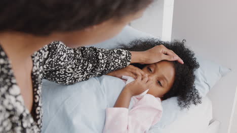 mother caring for sick daughter ill in bed with cold handing her a tissue