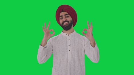 hombre indio sikh feliz mostrando la pantalla verde de la señal de ok