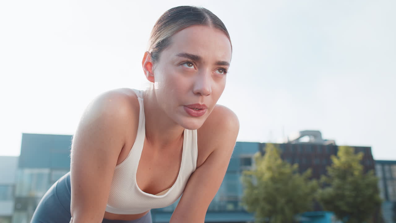 Tired young athlete woman jogger in sportswear resting after hard training in urban city park