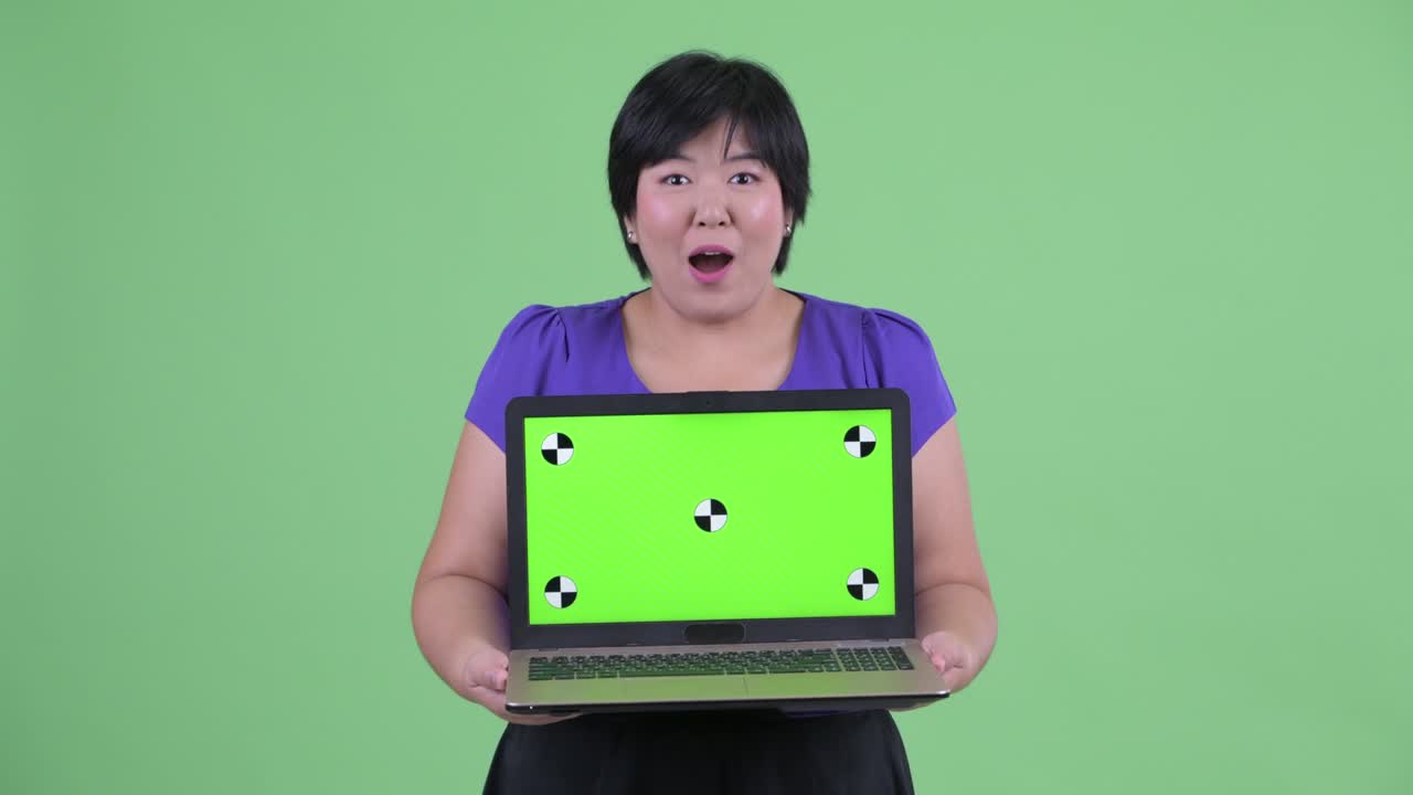 초록색 배경에 복사 공간을 가진 노트북을 들고 흥분하는 짧은 헤어 스타일을 가진 과체중 아시아 여성의 초상화