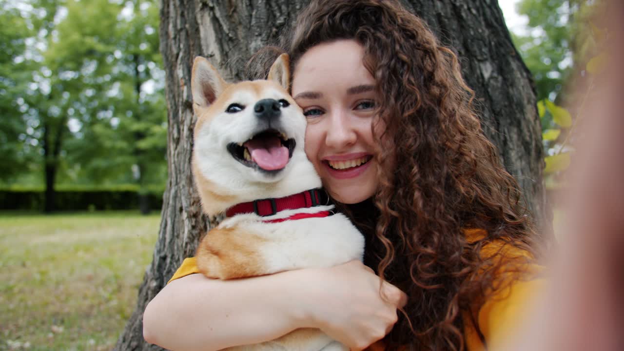 Close-up portrait of girl kissing dog in park taking selfie holding camera