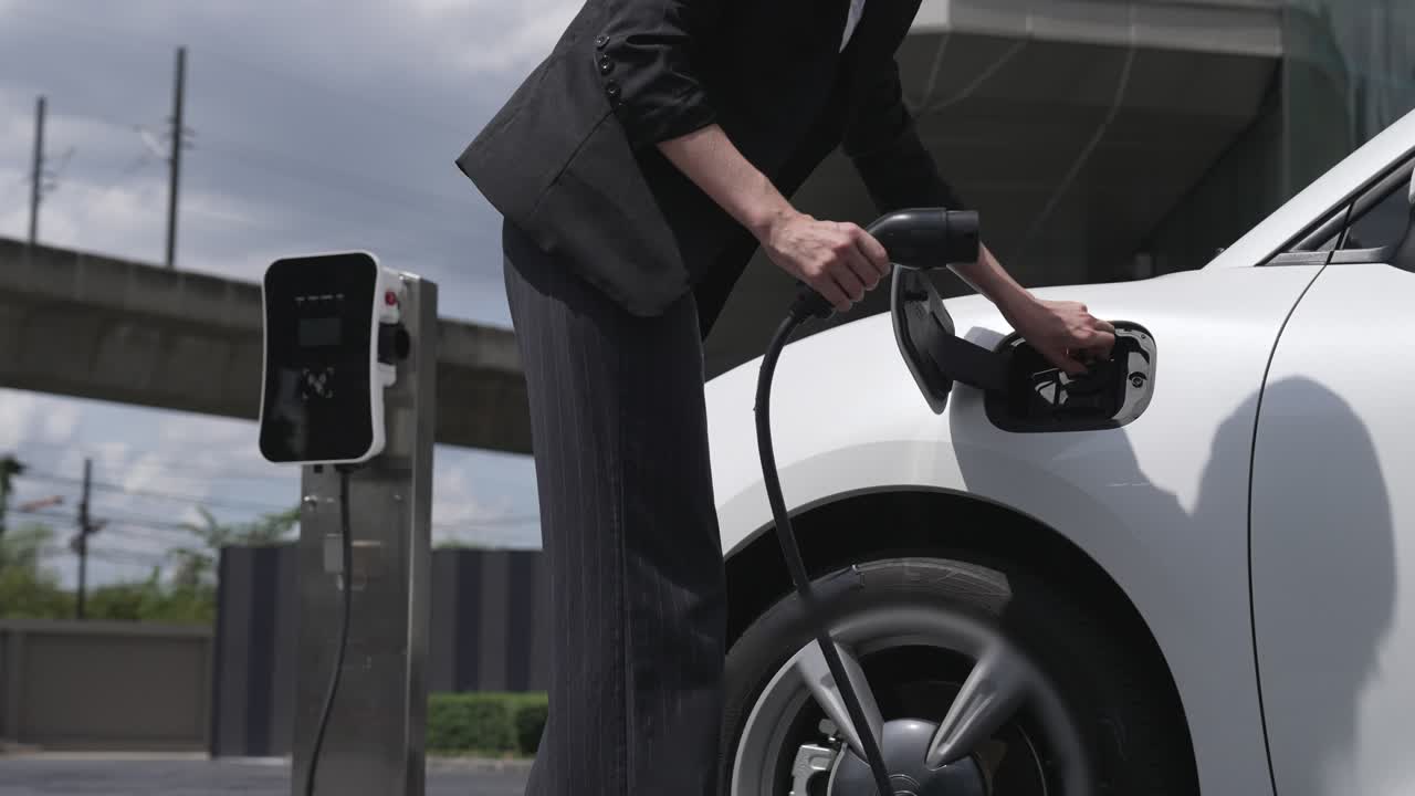 прогрессивная бизнес-женщина отключает зарядку от зарядной станции до своего автомобиля.