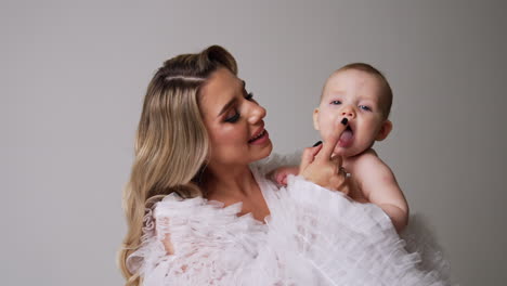 loving mother with her cute naked baby in hands. mom touches the cheeks and nose of her smiling kid.
