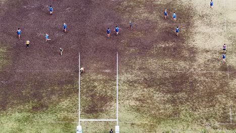 children engage in a lively rugby match on a muddy field, captured from above. overcast lighting and dynamic movement create an energetic atmosphere