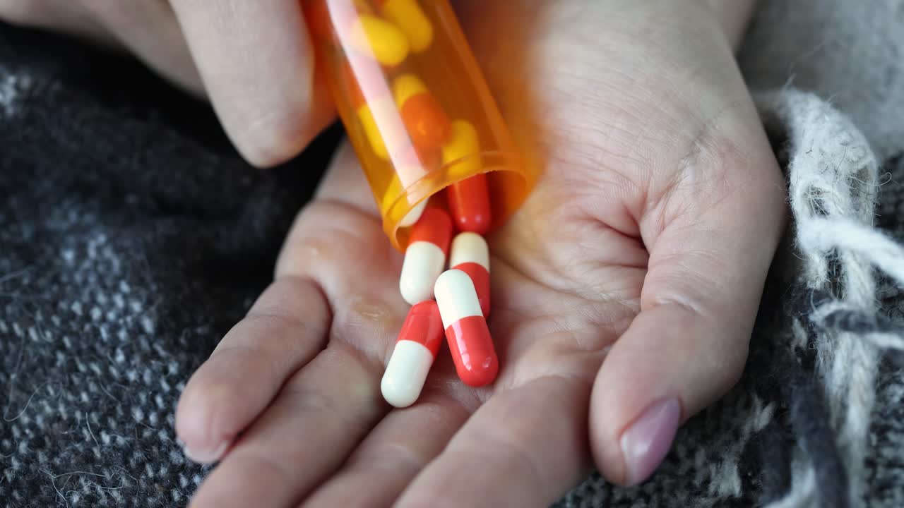 Una mano tiene una boccetta di farmaci mentre versa pillole gialle sul palmo.