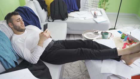 relaxed lazy man uses phone in his dirty and untidy home.