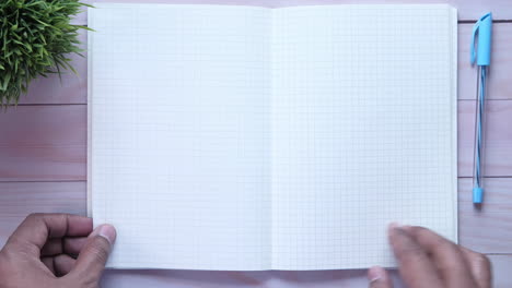 open notebook on wooden desk with pen and plant