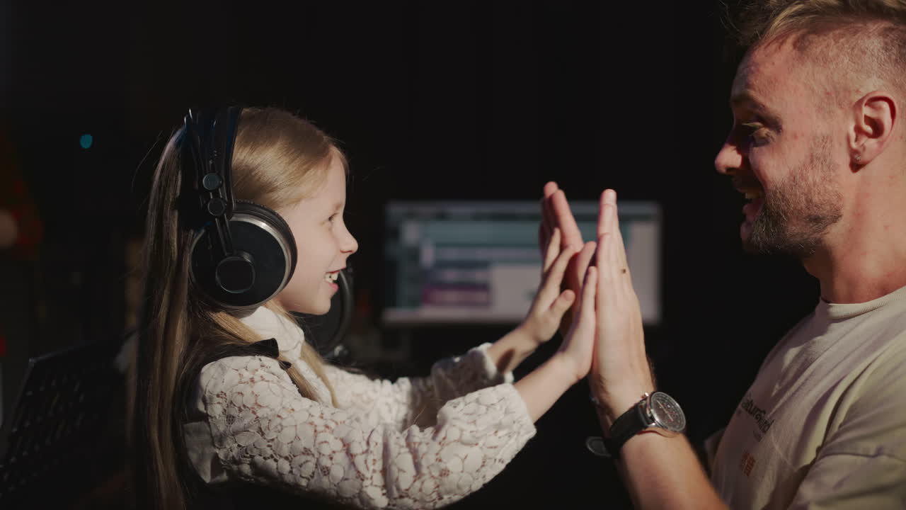 niño adolescente y hombre se regocijan en el estudio de grabación. niña sonriente juega con el maestro usando las manos durante el descanso de la lección vocal. entretenimiento en el estudio