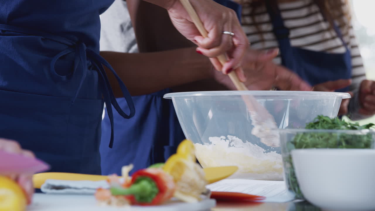 Nærbillede af kvinde, der blander ingredienser sammen i en skål til en opskrift på et madlavningskursus i et køkken.