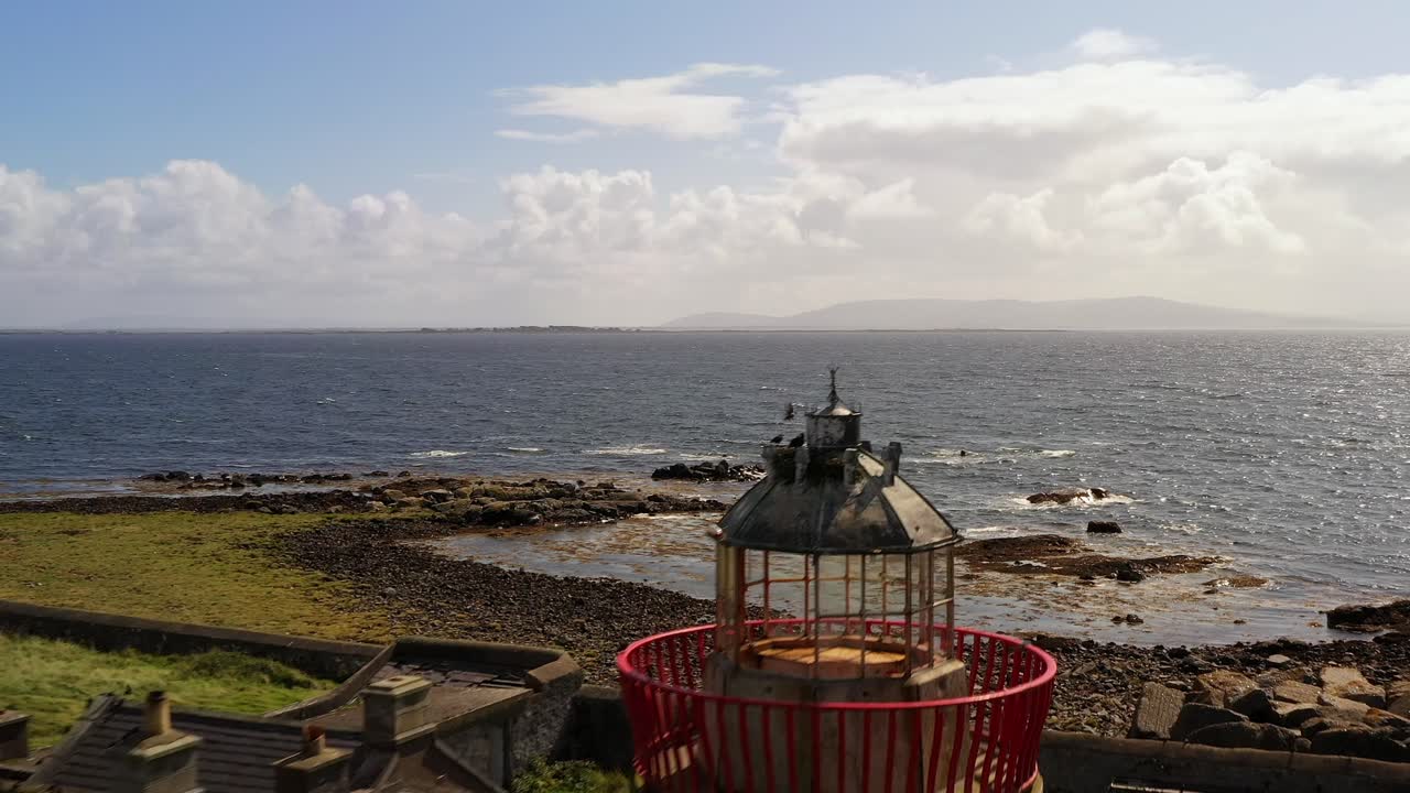 고각형 공중 도리 (high-angle aerial dolly) 는 아일랜드의 갈웨이 만 (galway bay) 에 어있는 거대한 바다와 함께 머튼 섬의 등대와 주변 구조물 위로 내려갑니다.