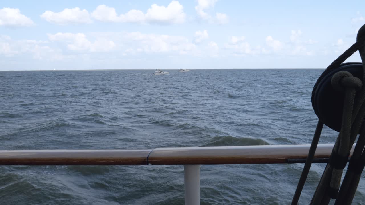 View of the sea with sailboats and motorboats in the distance, blue sky, white clouds, from a moving ship.