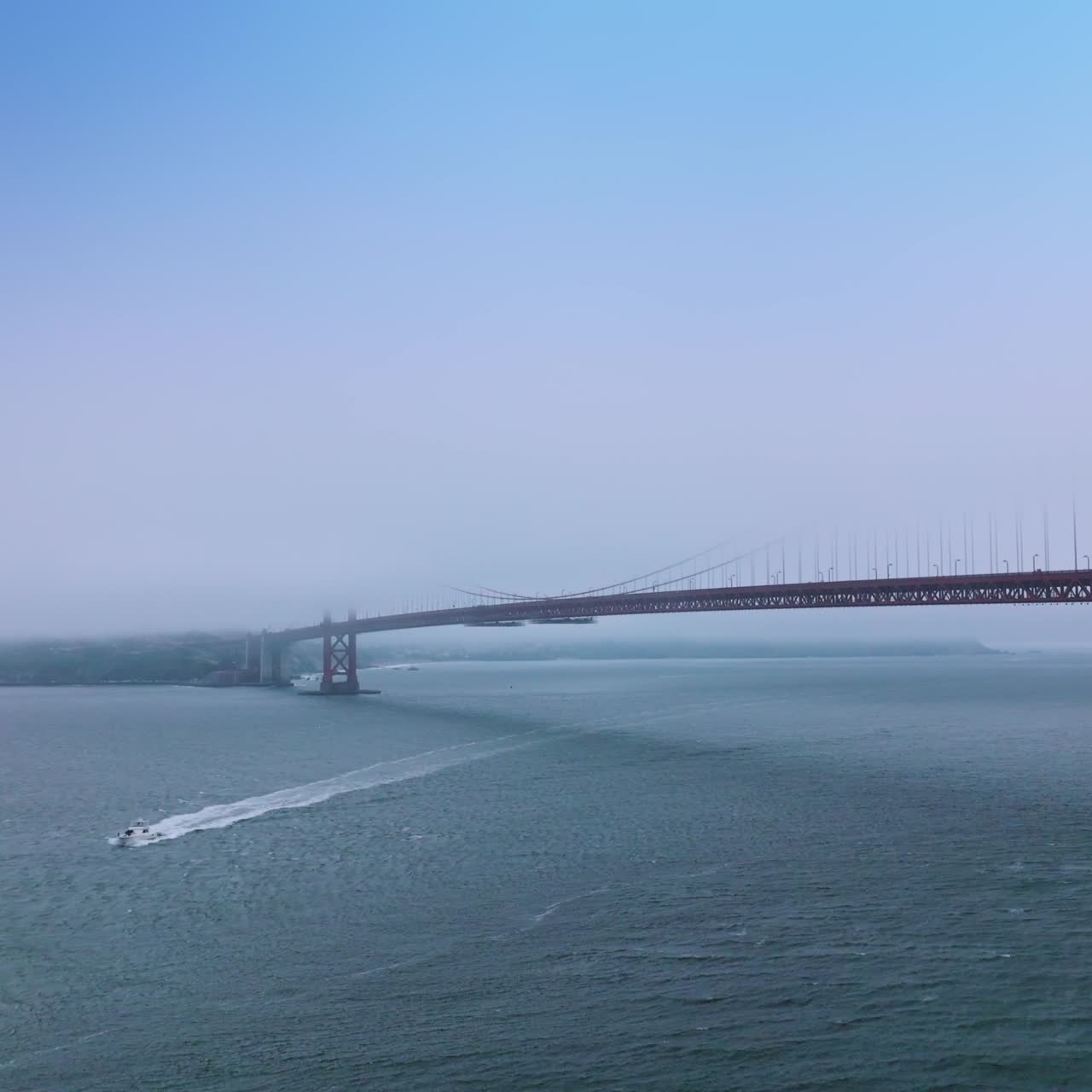 White yacht crossing the Golden Gate Straight in San Francisco, California, USA. Partial sight of namesake bridge hiding in the thick fog