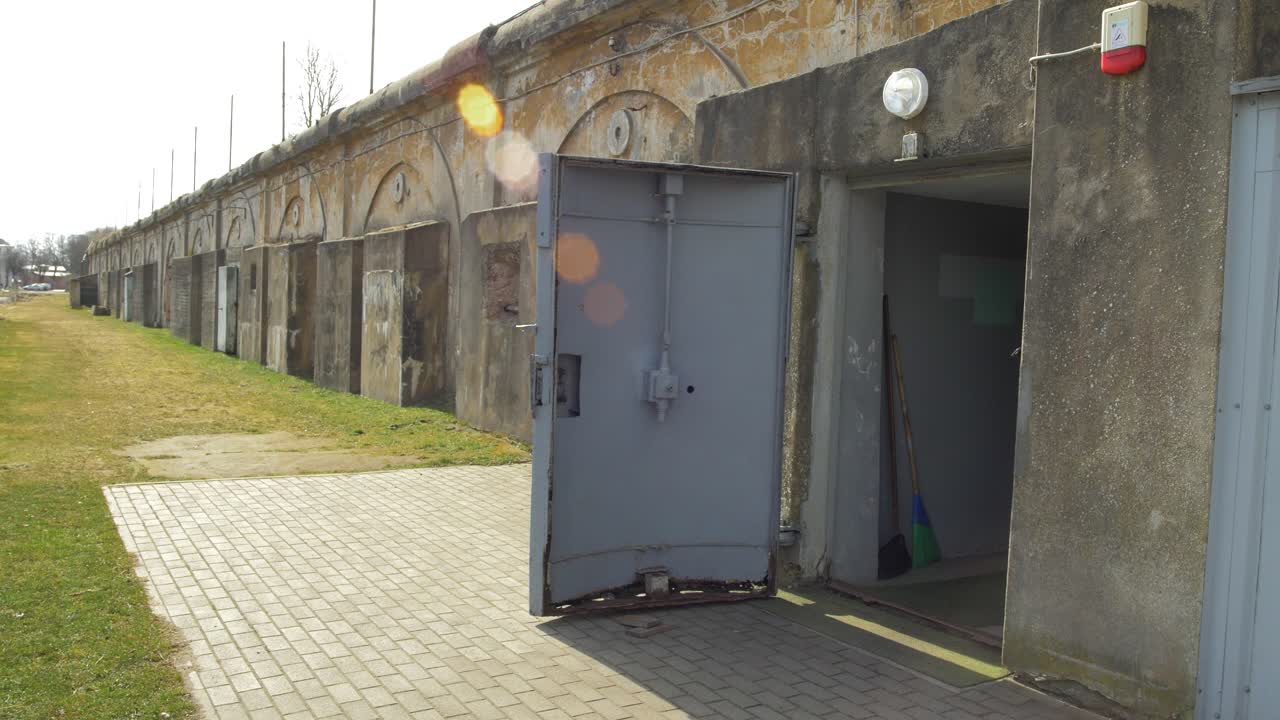 entrada con la puerta de acero en el refugio antibombas de hormigón para ocultar a la gente civil, un búnker subterráneo de apocalipsis construido en una antigua fortificación costera, día soleado, destello de lente, plano general