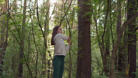 joven atleta estira los brazos en el bosque. jugando deportes rodeado de diferentes tipos de árboles en la naturaleza en un clima soleado. los rayos del sol caen sobre la dama