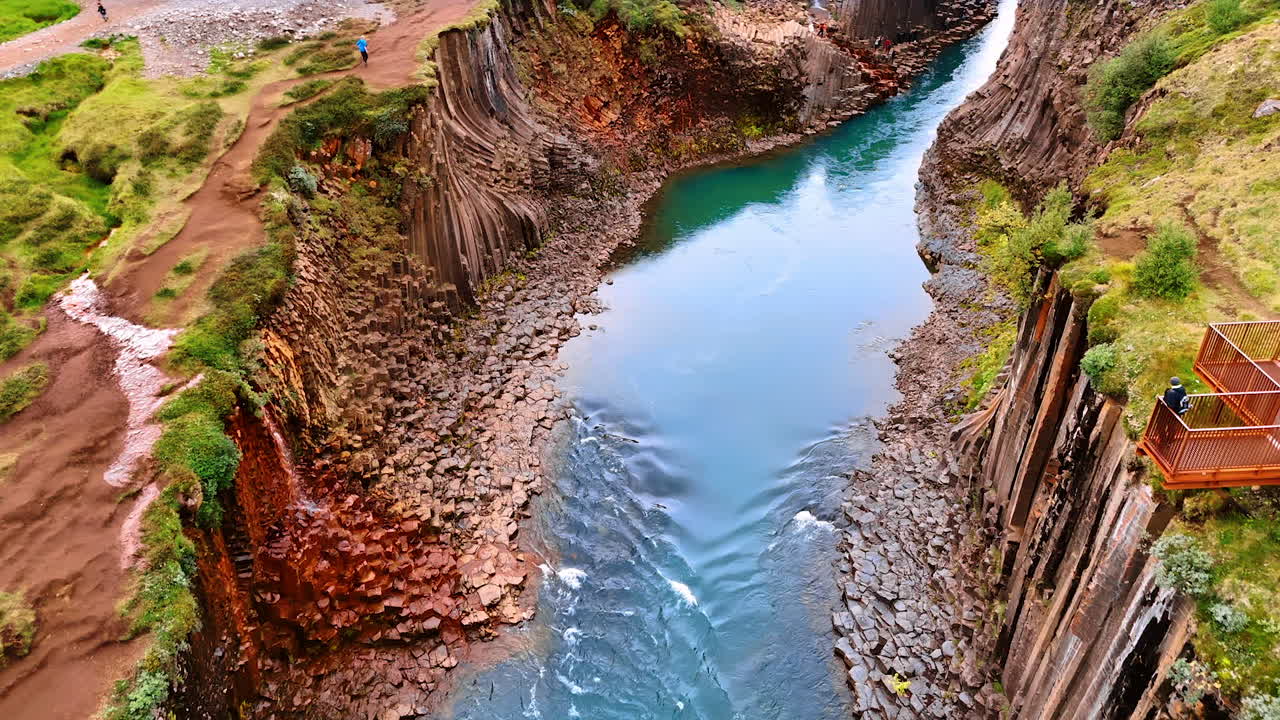 Flight above the river flowing in the crack among the rocks. Tourists walk by the rocky edge of mountains covered with moss. Iceland nature exploration.