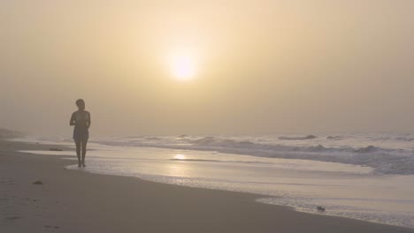 young female runs towards camera on a sandy seashore during sunset