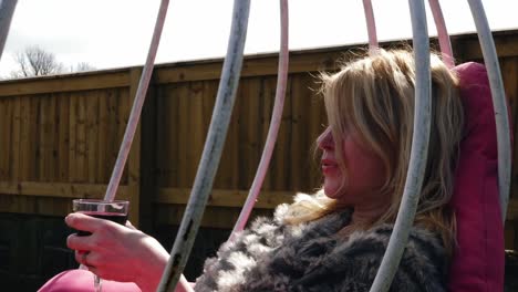 Attractive-woman-enjoys-glass-of-wine-in-garden-chair-swing-medium-zoom-slow-motion