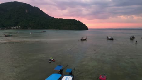 traditional thai longtail boats floating on calm water at sunset with dramatic sky in the background ascending drone