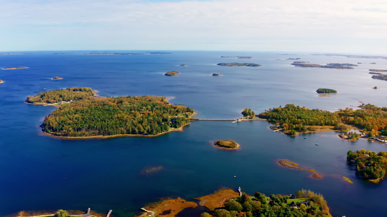 Aerial drone shot over the coastline of Oak Island, Nova Scotia, Canada.
High view of the sea, autumn colorful trees foliage. Picturesque landscape. Fall vibrant colors.