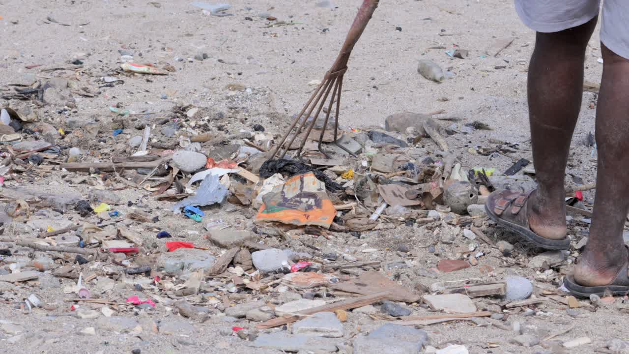 man collecting waste plastic with rake agriculture tool in Carter road beach mumbai india closeup shot
