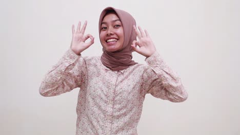 Excited-young-asian-muslim-woman-standing-pointing-down-and-showing-okay-hand-gesture