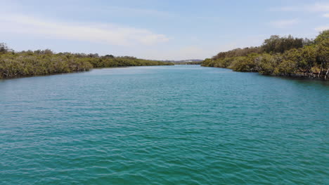 voando baixo em alta velocidade sobre a água azul clara do rio hastings na reserva natural da austrália, vista aérea