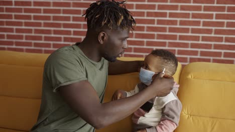 black dad putting on protective mask on son's face before walk