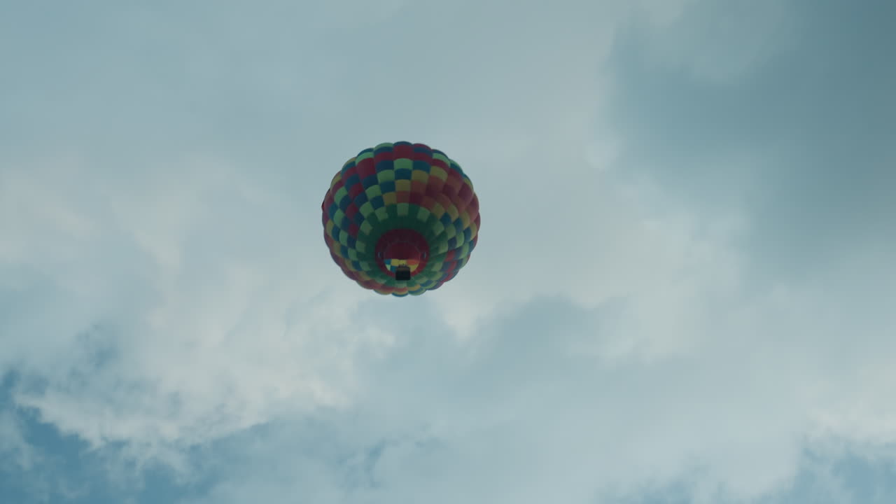 distant colorful patchwork hot air balloon ascending above open green field at dawn against clear sky invoking mood of peaceful aerial adventure and vast horizon view
