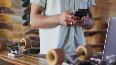 Video-Des-Mittelteils-Eines-Kaukasischen-Männlichen-Skateboarders,-Der-Sein-Smartphone-Im-Skateshop-Benutzt