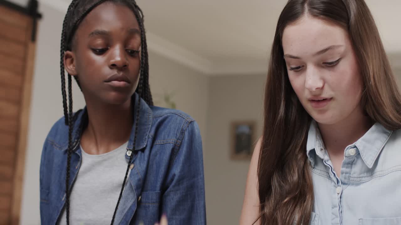 Focused diverse teenage female friends studying at home using computer and talking