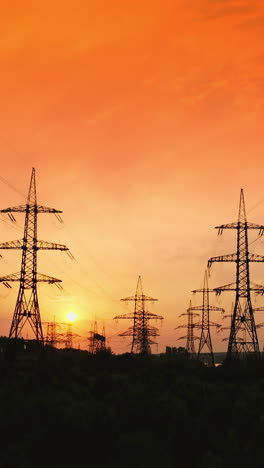 transmission lines against red evening sky. high-voltage electricity towers at sunset. silhouettes of electricity pylons and cables at beautiful orange sunset. motion camera back. vertical video