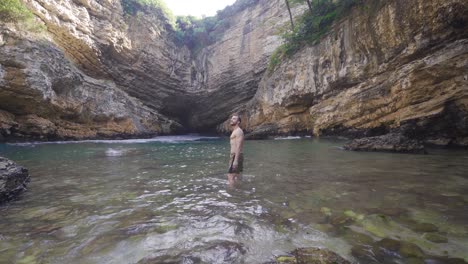 the young man walks through the water in the seaside cave with a fascinating view.