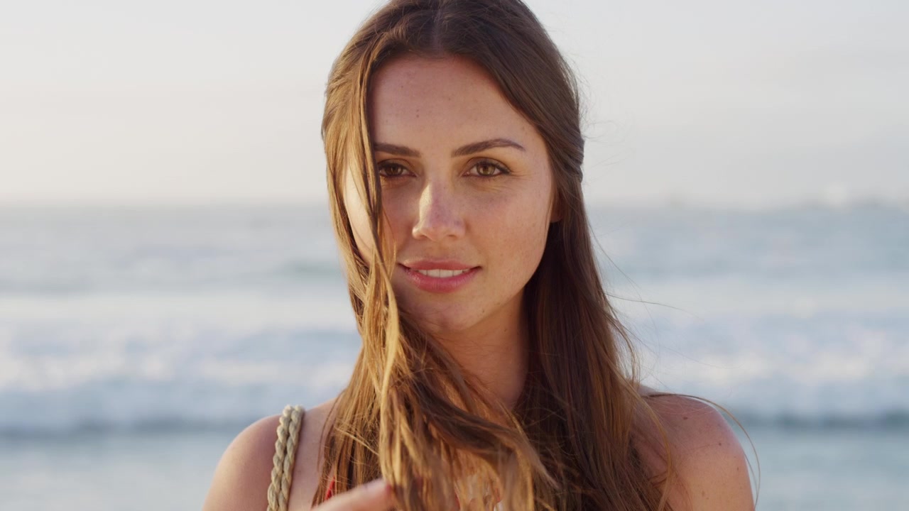 Giovane Donna che Sorride e si Tocca i Capelli in Spiaggia