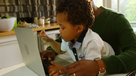 Vista-Lateral-De-Un-Joven-Padre-Negro-Y-Su-Hijo-Usando-Una-Computadora-Portátil-En-La-Mesa-Del-Comedor-En-La-Cocina-4k