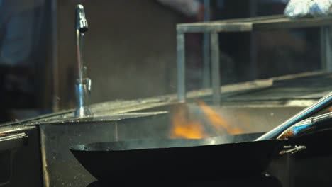 close interior static shot of two chefs next to each other ladling water while sauteing vegetables in a big wok on flames in restaurant at night