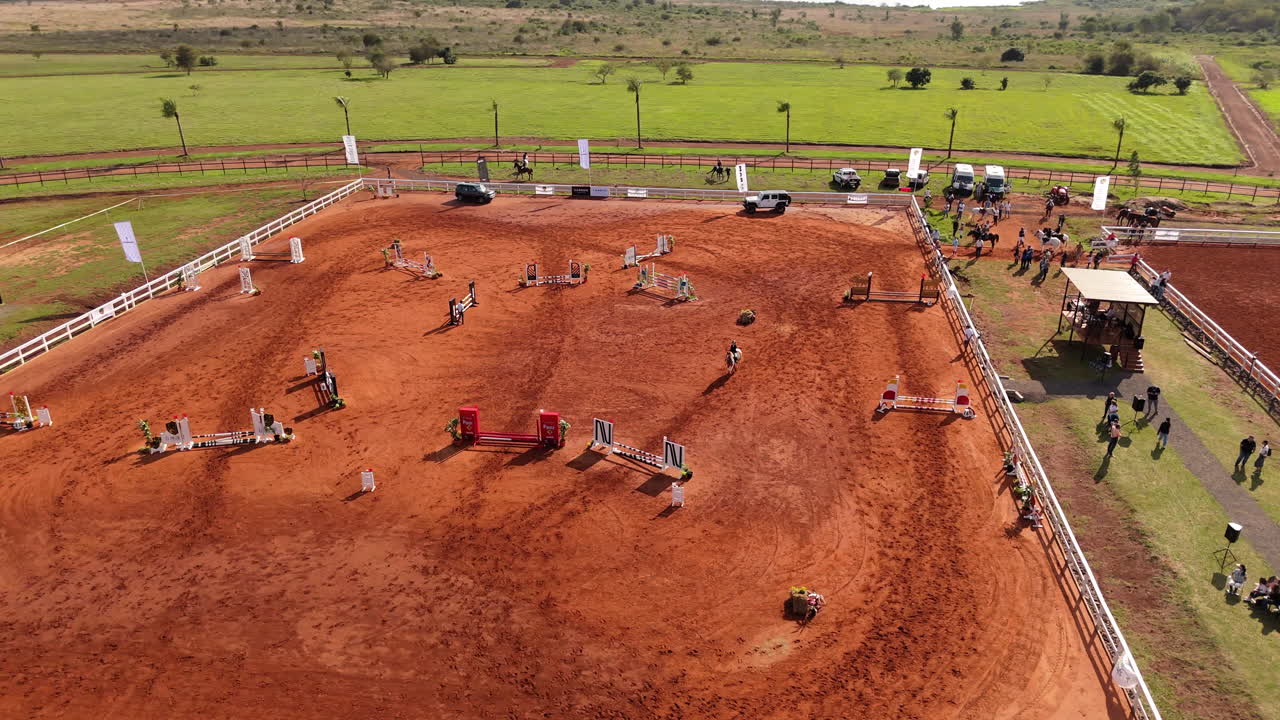 Equestrian arena with jumps set up, sunny weather, event spectators in background