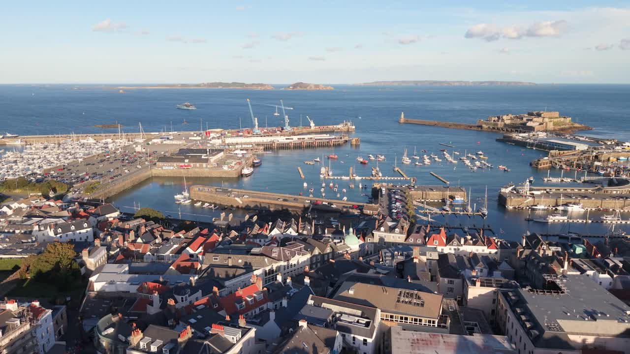 High flight over rooftops of St Peter Port Guernsey towards harbour Herm Sark and Jethou in the distance in bright afternoon sunshine on calm day