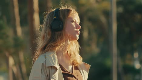 young woman closes eyes listening to inspirational podcast outdoors at sunset