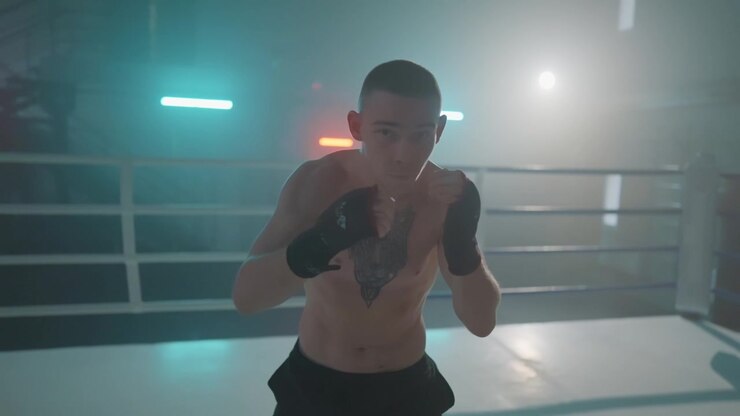 Giovane pugile che si allena e fa shadow boxing in un ring illuminato in modo suggestivo.