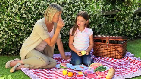 una mujer joven y su hija comiendo frutas en el jardín