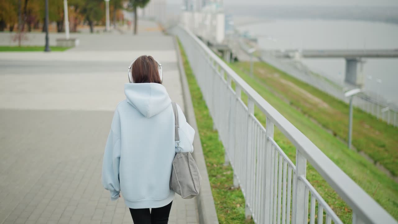 Lady walking along street with blurred view of bridge, river, and street lights in background, serene outdoor setting, casual walk, peaceful environment, cityscape with nature