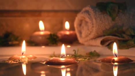 relaxing spa background with candles floating in the bath water, some green petals and a towel near the water surface