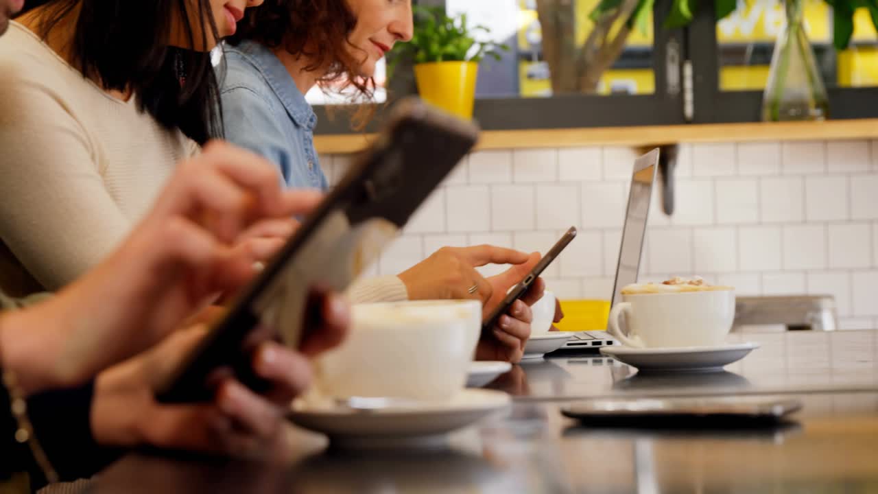 Colleagues tapping devices at cafe counter, starting bar chart and globe overlays showing tech data